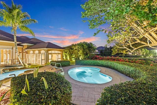 pool at dusk featuring a patio and a jacuzzi