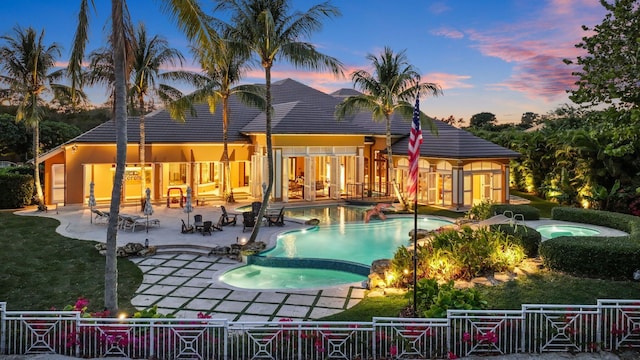 pool at dusk with an in ground hot tub and a patio area