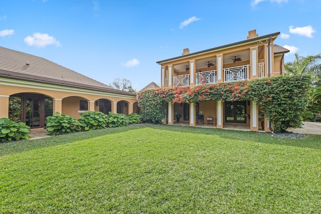 rear view of house with a yard, a balcony, french doors, and ceiling fan