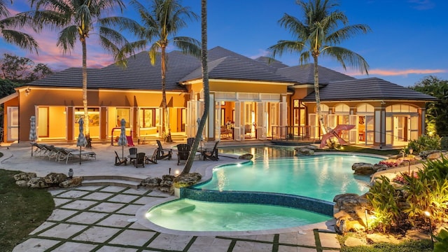 pool at dusk featuring an in ground hot tub and a patio area