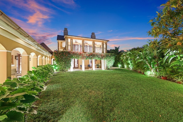 back house at dusk with a lawn and a balcony