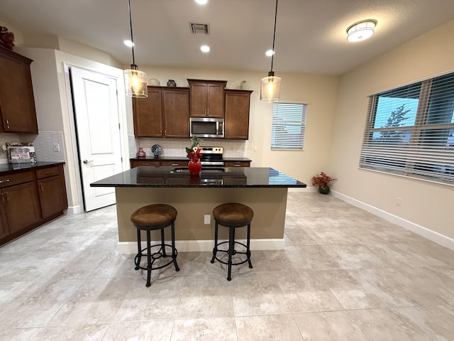 kitchen featuring hanging light fixtures, appliances with stainless steel finishes, dark stone counters, and a kitchen island