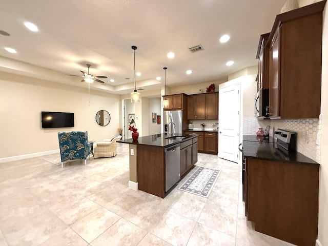 kitchen featuring a center island with sink, ceiling fan, stainless steel appliances, backsplash, and decorative light fixtures