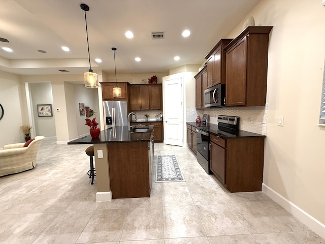 kitchen with decorative light fixtures, backsplash, sink, a kitchen island with sink, and stainless steel appliances