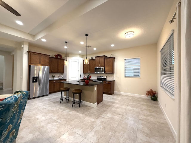 kitchen with a center island with sink, a breakfast bar, hanging light fixtures, appliances with stainless steel finishes, and light tile patterned floors