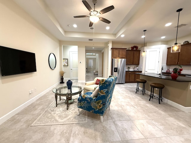 tiled living room with ceiling fan and a raised ceiling