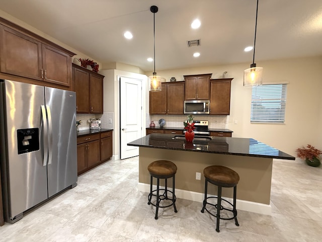 kitchen with dark stone counters, appliances with stainless steel finishes, a kitchen island, and decorative light fixtures