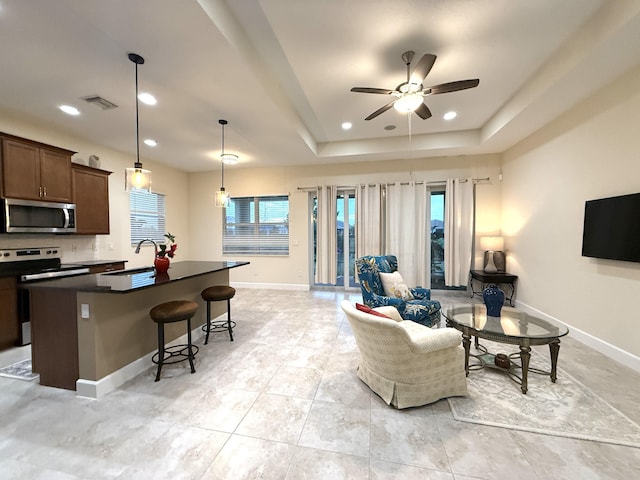 living room with ceiling fan, a tray ceiling, and sink