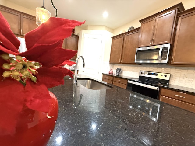 kitchen with stainless steel appliances, decorative backsplash, dark stone counters, pendant lighting, and sink