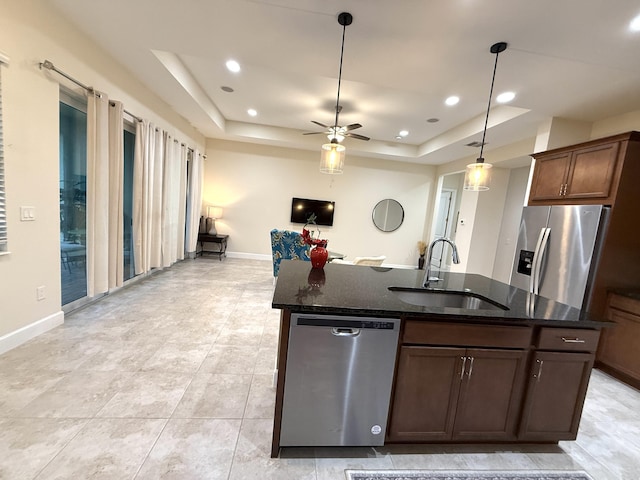 kitchen with a raised ceiling, sink, stainless steel appliances, and a center island with sink