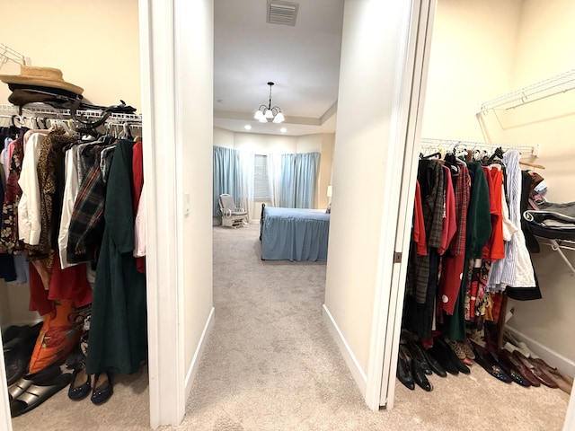 spacious closet featuring light carpet, a notable chandelier, and a tray ceiling