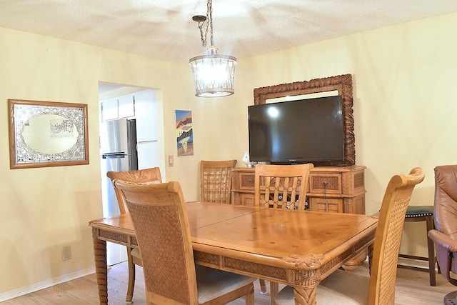 dining room featuring light wood-type flooring, an inviting chandelier, and a textured ceiling