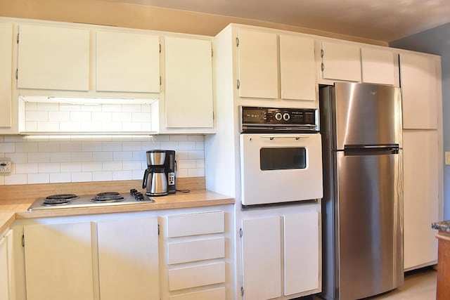 kitchen with oven, decorative backsplash, gas stovetop, white cabinets, and stainless steel fridge