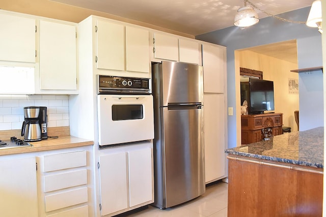 kitchen featuring dark stone countertops, decorative backsplash, stainless steel fridge, oven, and light tile patterned flooring