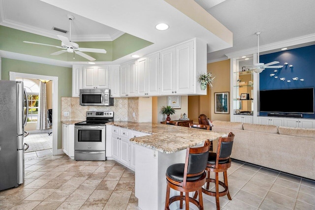 kitchen with kitchen peninsula, stainless steel appliances, white cabinetry, and a breakfast bar