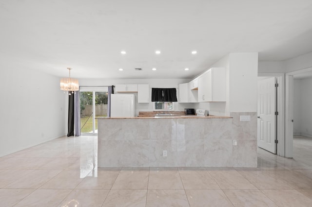 kitchen with white fridge, kitchen peninsula, an inviting chandelier, hanging light fixtures, and white cabinets