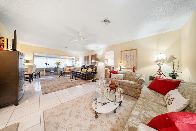 living room with ceiling fan, a textured ceiling, and light tile patterned flooring