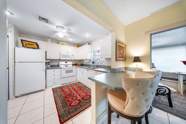 kitchen with ceiling fan, white appliances, a textured ceiling, white cabinets, and a breakfast bar