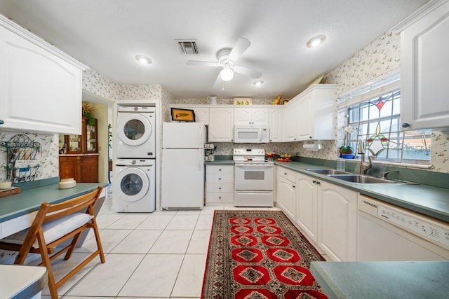 kitchen featuring stacked washer / drying machine, sink, white appliances, light tile patterned flooring, and white cabinets