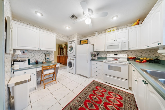 kitchen with white appliances, white cabinets, stacked washer and clothes dryer, ceiling fan, and light tile patterned floors