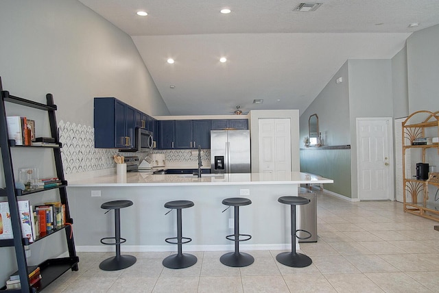 kitchen featuring kitchen peninsula, blue cabinets, a breakfast bar, high vaulted ceiling, and stainless steel appliances