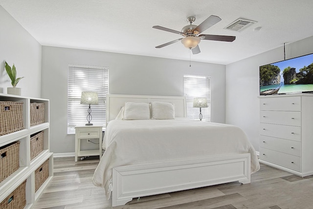 bedroom with ceiling fan, light hardwood / wood-style floors, and a textured ceiling