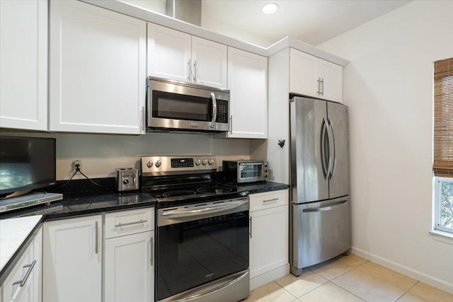 kitchen featuring dark stone countertops, light tile patterned floors, stainless steel appliances, and white cabinets