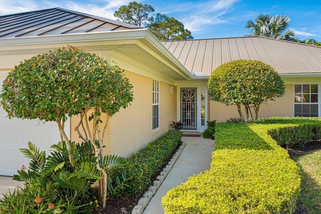 entrance to property with a garage, a standing seam roof, metal roof, and stucco siding