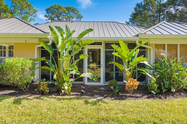 view of property exterior featuring a yard, stucco siding, a sunroom, a standing seam roof, and metal roof