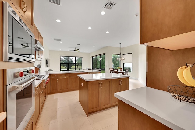 kitchen featuring appliances with stainless steel finishes, decorative light fixtures, sink, a center island, and kitchen peninsula