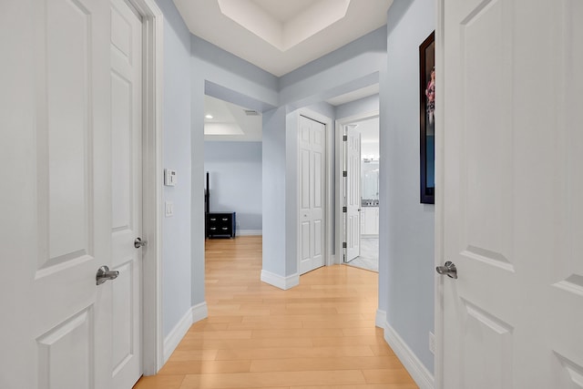 hallway featuring a raised ceiling and light hardwood / wood-style flooring