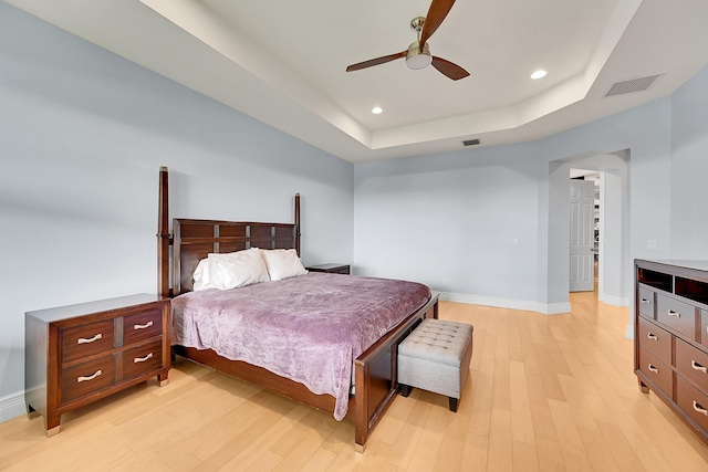 bedroom with ceiling fan, a raised ceiling, and light hardwood / wood-style flooring