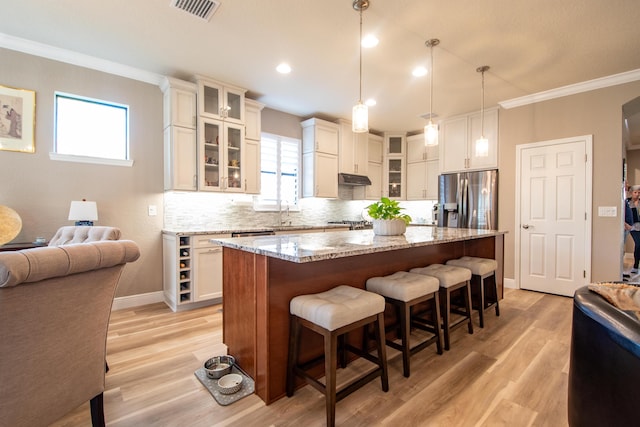 kitchen with light stone countertops, a kitchen breakfast bar, a kitchen island, pendant lighting, and stainless steel fridge