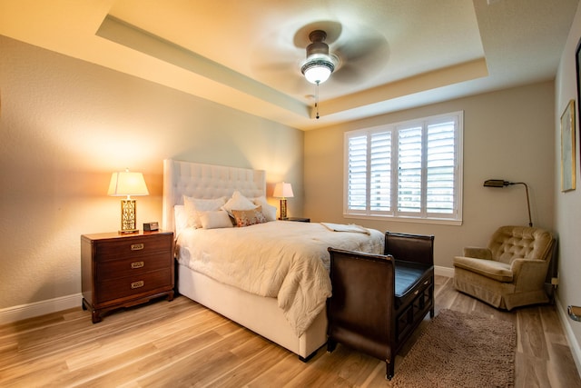 bedroom featuring ceiling fan, light hardwood / wood-style floors, and a tray ceiling