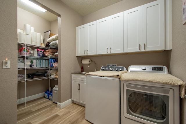 clothes washing area featuring sink, light wood-type flooring, cabinets, a textured ceiling, and washer and clothes dryer