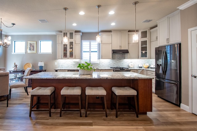 kitchen with stainless steel fridge with ice dispenser, a kitchen island, a breakfast bar area, and decorative light fixtures