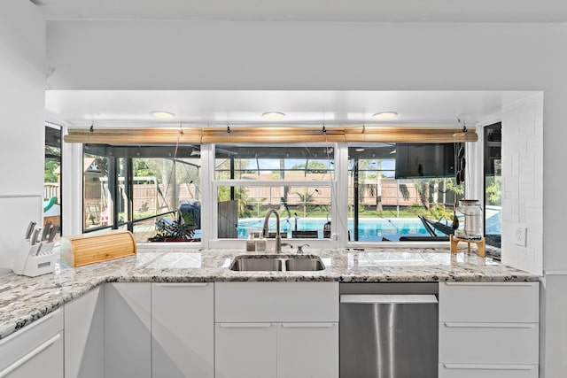 kitchen featuring light stone countertops, a sink, white cabinets, and a healthy amount of sunlight