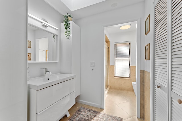 full bath with wainscoting, toilet, tile patterned floors, vanity, and tile walls