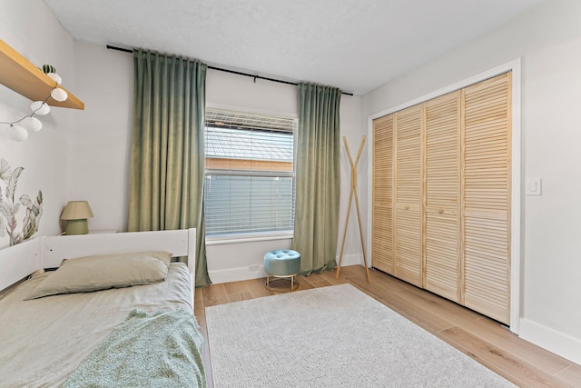 bedroom with a closet, a textured ceiling, baseboards, and wood finished floors