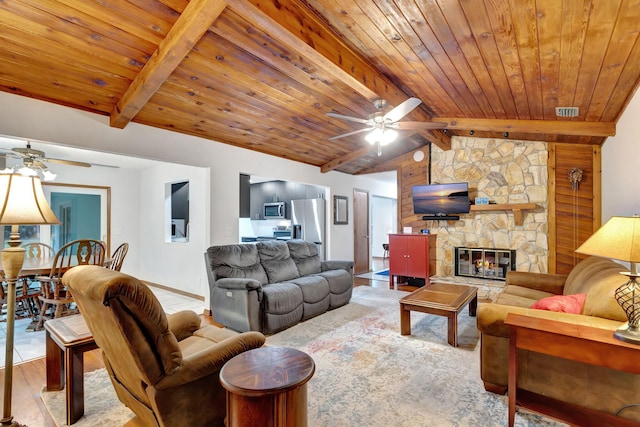 living room with ceiling fan, wooden ceiling, a stone fireplace, and vaulted ceiling with beams