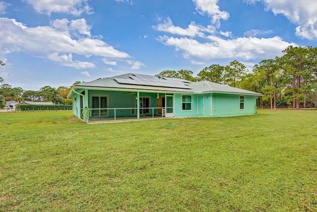 rear view of property featuring a lawn, a sunroom, and solar panels