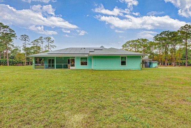 rear view of house featuring a sunroom, a yard, and solar panels