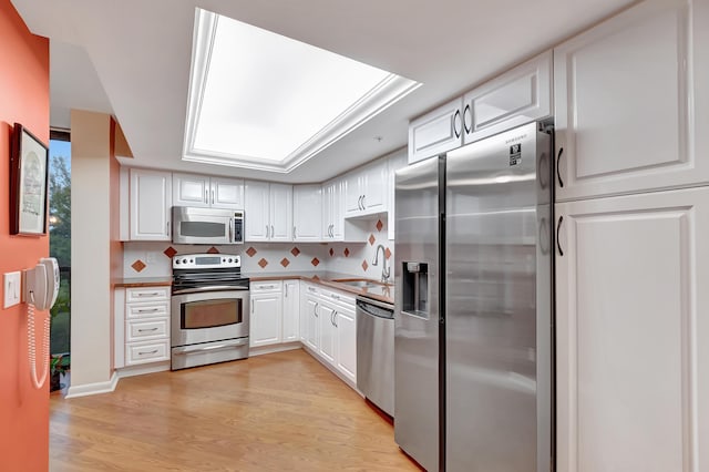 kitchen with light hardwood / wood-style flooring, appliances with stainless steel finishes, sink, white cabinets, and tasteful backsplash