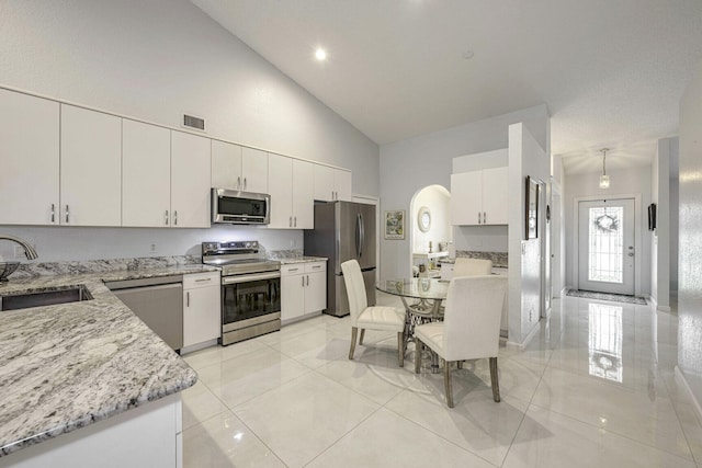 kitchen with appliances with stainless steel finishes, white cabinetry, sink, high vaulted ceiling, and light stone counters