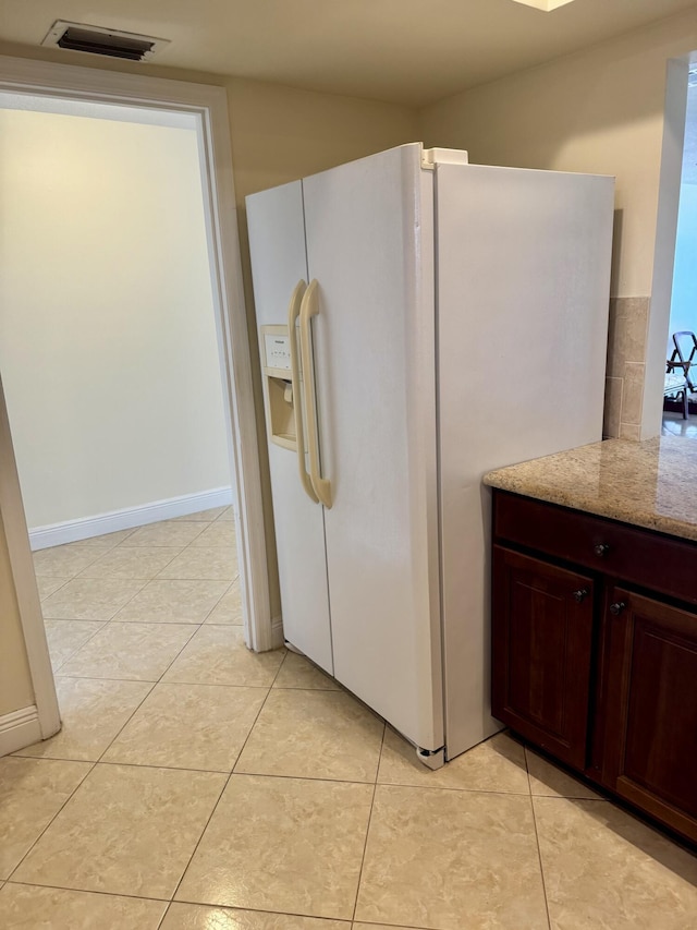 kitchen with white refrigerator with ice dispenser, light stone countertops, and light tile patterned flooring