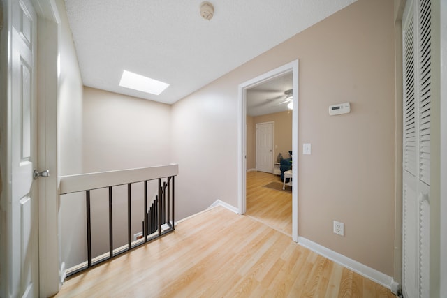 corridor featuring light hardwood / wood-style floors, a textured ceiling, and a skylight