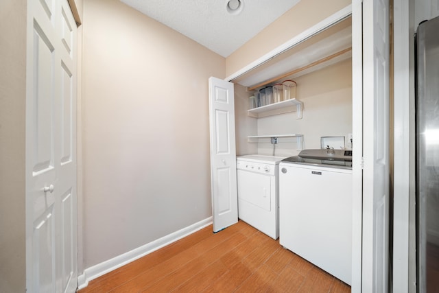 clothes washing area with light wood-type flooring, a textured ceiling, and washer and clothes dryer