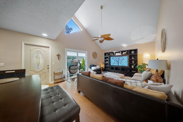 living room featuring ceiling fan, a textured ceiling, light wood-type flooring, and vaulted ceiling