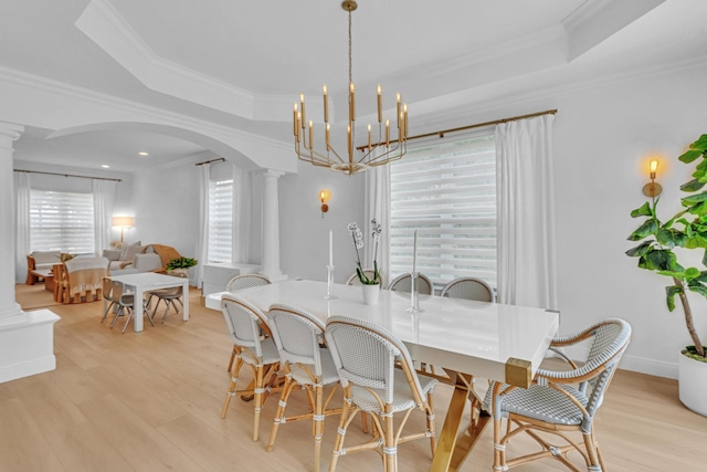 dining space featuring a raised ceiling, light hardwood / wood-style flooring, and ornate columns