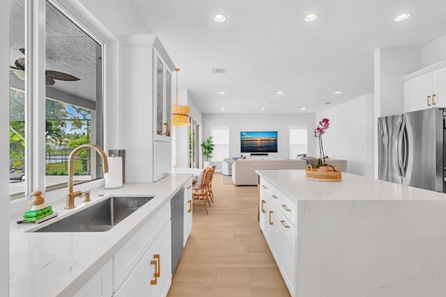 kitchen with sink, light hardwood / wood-style flooring, appliances with stainless steel finishes, a kitchen island, and white cabinets